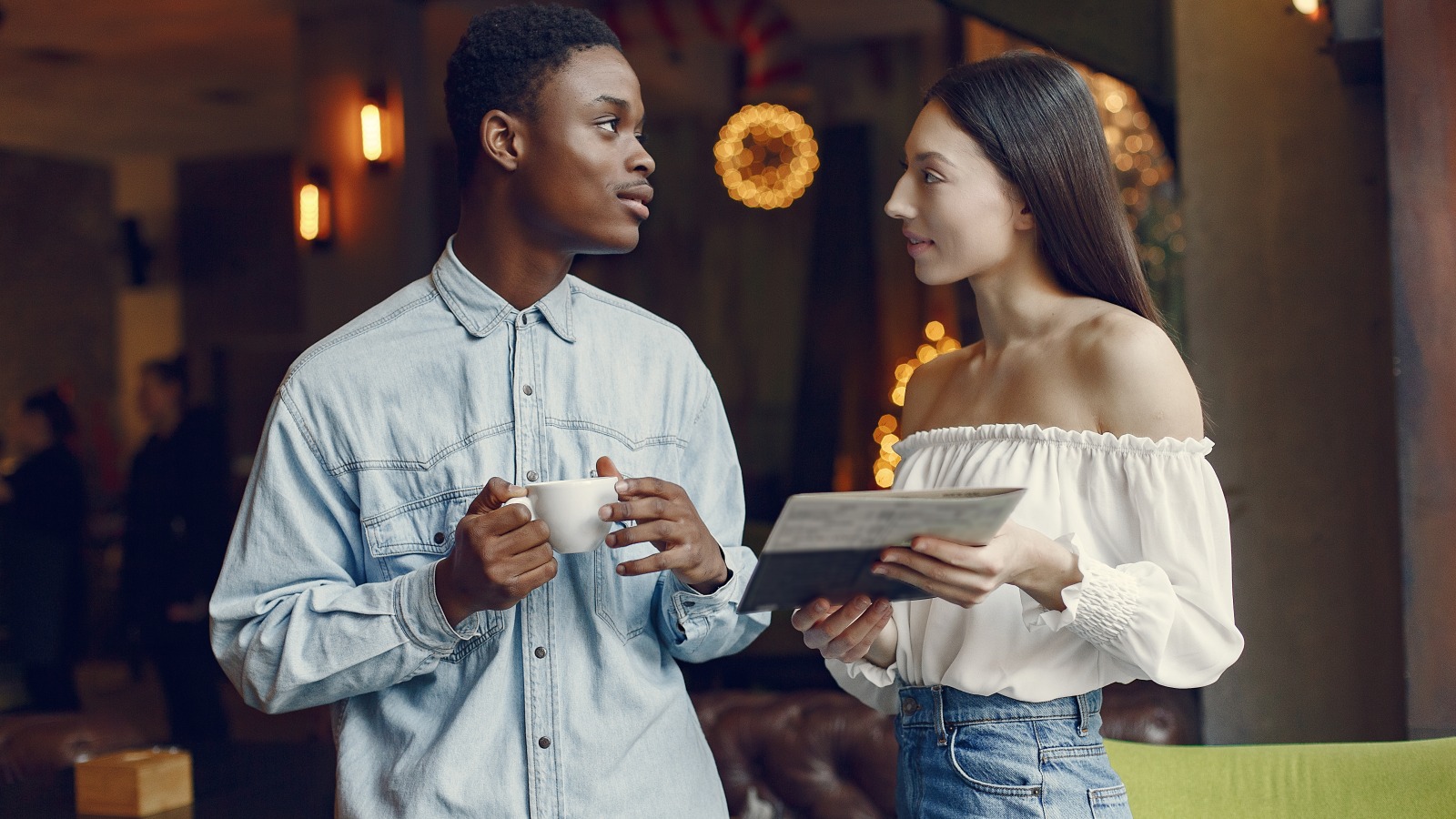Two young professionals chatting over coffee at an evening meetup in a warmly lit cafe