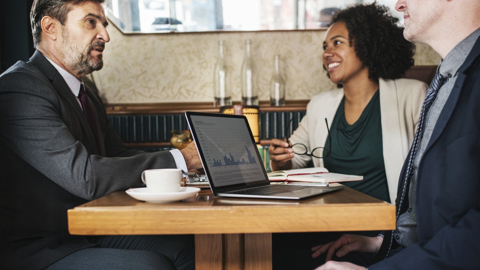 Three people talking over a laptop and coffee at a wooden cafe table
